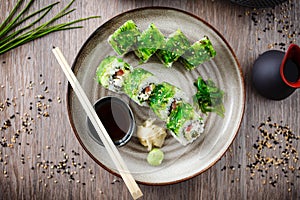 Sushi maki rolls with cucumber, avocado, tomato, creamy cheese, chuka wakame on a plate with chopsticks, soy sauce