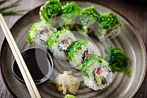 Sushi maki rolls with cucumber, avocado, tomato, creamy cheese, chuka wakame on a plate with chopsticks, soy sauce