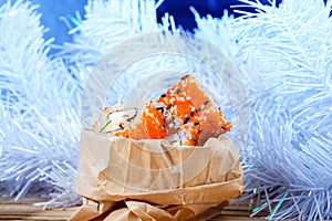 Sushi olla in an unusual New Year packaging, against a white Christmas tree.