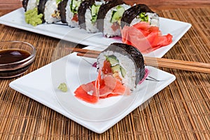 Sushi on plates, condiments, chopsticks on bamboo table mat closeup