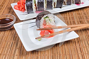 Sushi on rectangular plates, condiments, chopsticks on bamboo table mat