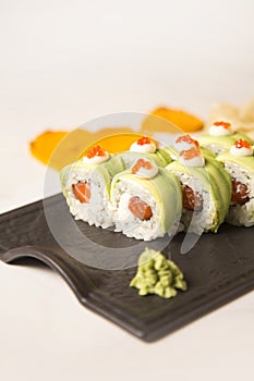 Sushi roll with avocado slices, red caviar on top on black plate, marble background