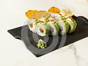 Sushi roll with avocado slices, red caviar on top on black plate, marble background