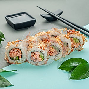 Sushi roll Bonito in tuna shavings. With fried salmon and cucumber. Decorated with greenery. In the background is a gravy boat and