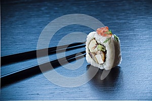 Sushi roll with caviar and chopsticks on black tableboard. Japanese food concept.