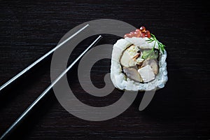 Sushi roll with caviar and chopsticks on black tableboard top view. Japanese food concept.