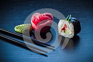 Sushi roll with caviar, ginger, wassabi and chopsticks on black tableboard. Japanese food concept.