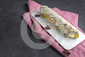 Sushi roll with chopsticks on a white plate. Pink napkin on a gray background and anise