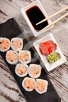 Sushi roll covered with chopped salmon and caviar is served on rectangular black slate.