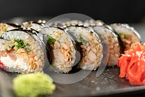 sushi roll futomaki with cucumber and fried salmon on a black stone plate.