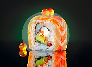 Sushi roll over black background. California sushi roll with salmon, vegetables, flying fish roe closeup