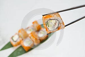 Sushi Roll piece wrapped in rice and flying fish roe Tobiko, Masago caviar hold in metal chopsticks