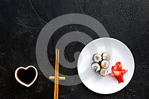 Sushi roll with salmon and avocado on plate with soy sauce, chopstick, wasabi on black background top view copyspace