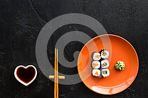 Sushi roll with salmon and avocado on plate with soy sauce, chopstick, wasabi on black background top view copyspace