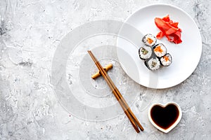 Sushi roll with salmon and avocado on plate with soy sauce, chopstick, wasabi on grey stone background top view
