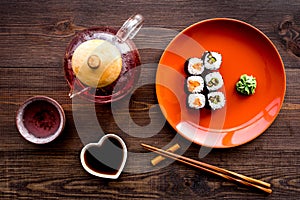 Sushi roll with salmon and avocado on plate with soy sauce, chopstick, wasabi on wooden table background top view