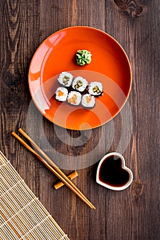 Sushi roll with salmon and avocado on plate with soy sauce, chopstick, wasabi on wooden table background top view