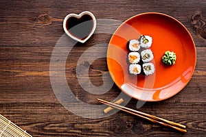 Sushi roll with salmon and avocado on plate with soy sauce, chopstick, wasabi on wooden table background top view