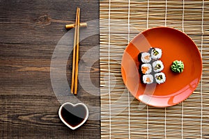 Sushi roll with salmon and avocado on plate with soy sauce, chopstick, wasabi on wooden table background top view