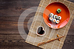 Sushi roll with salmon and avocado on plate with soy sauce, chopstick, wasabi on wooden table background top view