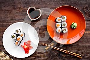 Sushi roll with salmon and avocado on plate with soy sauce, chopstick, wasabi on wooden table background top view