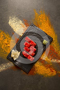 Sushi roll with salmon, red flying fish roe Tobiko with wasabi, ginger on black plate, Scattered spices on background