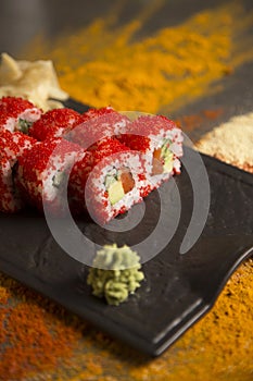 Sushi roll with salmon, red flying fish roe Tobiko with wasabi, ginger on black plate, Scattered spices on background