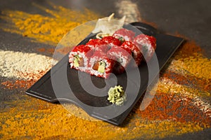 Sushi roll with salmon, red flying fish roe Tobiko with wasabi, ginger on black plate, Scattered spices on background