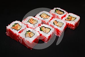 Sushi roll with scrambled eggs, salmon, in red masago caviar on a black background.