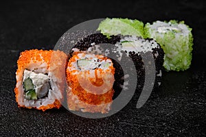 Sushi roll with shrimp inside and flying fish roe on top on black background