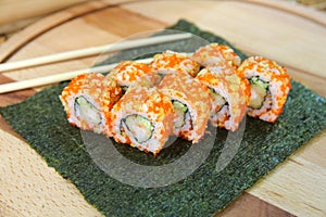 Sushi roll with tempura shrimp served on nori seaweed sheet with chopsticks near dish