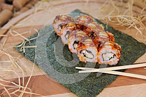 Sushi roll with unagi eel served on nori seaweed sheet with chopsticks near dish served with sauce