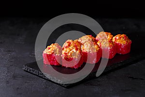 Sushi rolls with grilled salmon, rice, nori, creamy cheese, cucumber and masago on a black background