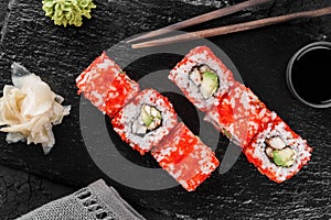 Sushi rolls and maki set with smoked eel, cream cheese, avocado, red caviar and wasabi on black slate background.