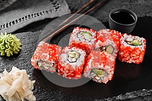 Sushi rolls and maki set with smoked eel, cream cheese, avocado, red caviar and wasabi on black slate background. Japanese cuisine