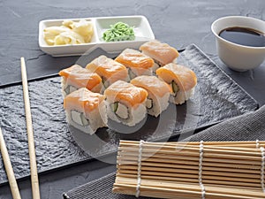 Sushi rolls philadelphia on a black textured plate stand on a gray background. wasabi ginger and sauce chopsticks. Rolls with