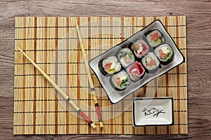 Sushi rolls on a plate on bamboo brown straw mat with chopsticks close up
