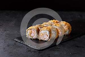 Sushi rolls with rice, nori, spicy sauce, cucumber, shrimp, masago on a black slate