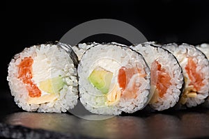 Sushi Rolls with salmon, avocado, omelet and Cream Cheese inside. Maki Futomaki Sushi Rolls with salmon on black background. Sushi