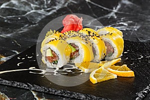 Sushi Rolls with salmon, avocado, omelet inside and mango on top. Sushi Rolls with salmon on black marble background. Sushi menu.