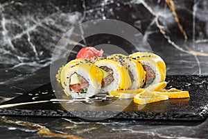 Sushi Rolls with salmon, avocado, omelet inside and mango on top. Sushi Rolls with salmon on black marble background. Sushi menu.