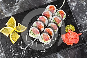 Sushi Rolls with salmon, avocado, tuna and cucumber inside. Maki Futomaki Sushi Rolls with salmon on black marble background .