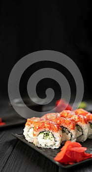 Sushi rolls with salmon, caviar, cucumber and cream cheese on a black plate on a dark background. Japanese food. Sushi