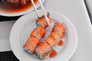 Sushi rolls set. Hand with chopsticks for sushi over white plate. Food at chinese buffet restaurant