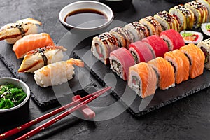 Sushi rolls set, nigiri sushi and soy sauce on a black textured background and chopsticks on the side.