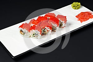 Sushi rolls set with red caviar and cream cheese served on a white plate over black background.