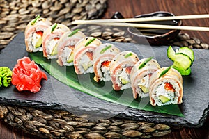 Sushi rolls set with salmon, cream cheese, red caviar, avocado and wasabi on black stone on bamboo mat, selective focus.