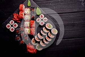 Sushi rolls set served with wasabi and ginger on a black wood table