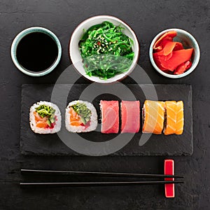 Sushi rolls set, soy sauce, seaweed salad and chopsticks from below on black slate board