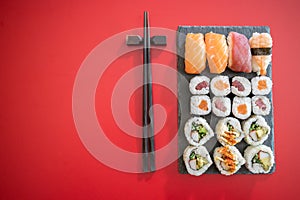 Sushi rolls set with tuna and salmon fish and black chopsticks isolated on red background